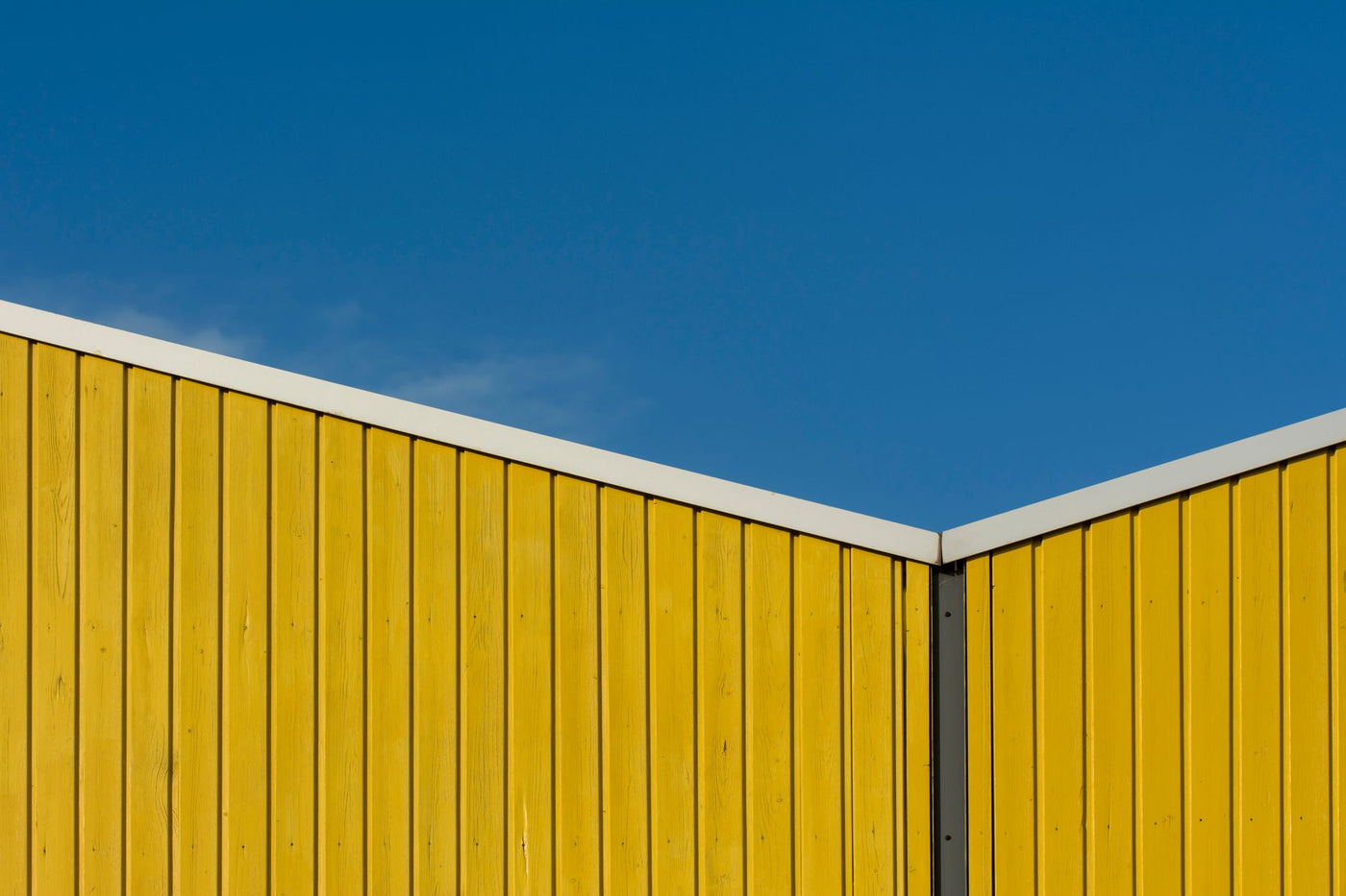 A striking minimalist photo of a yellow building facade against a clear blue sky.