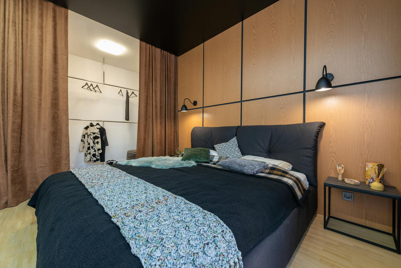 Modern interior of bedroom furnished with bed with cushions near bedside and closet with clothes