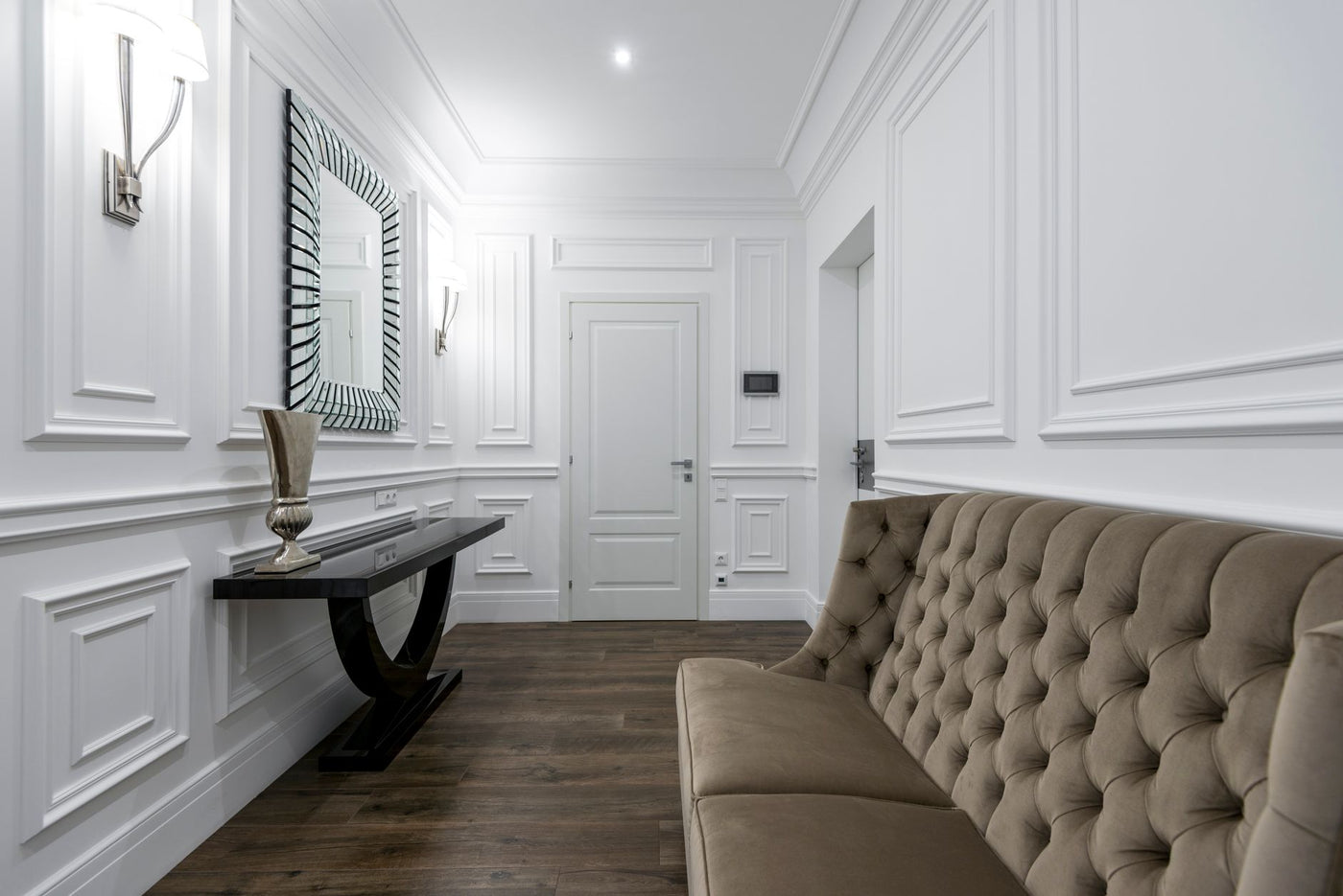 Luxurious white interior featuring a modern tufted sofa and classic wall paneling.