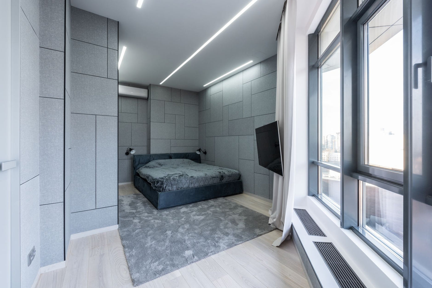Interior of modern light apartment with bed near carpet with TV near windows and curtains in day
