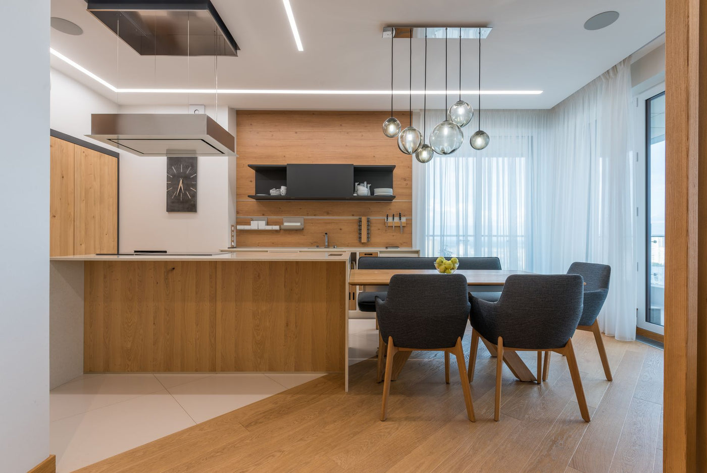 Interior of contemporary kitchen with wooden furniture and floor and dining table with soft chairs in cozy apartment