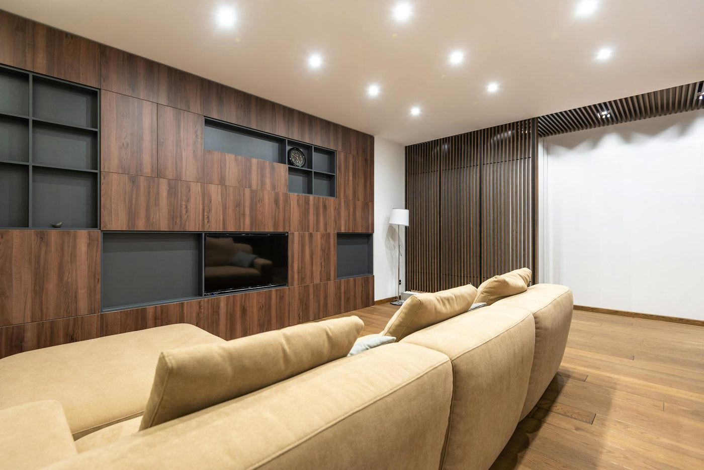 Soft sofa with cushions placed near decorative black shelves in stylish light spacious apartment with decorative wooden partitions at home