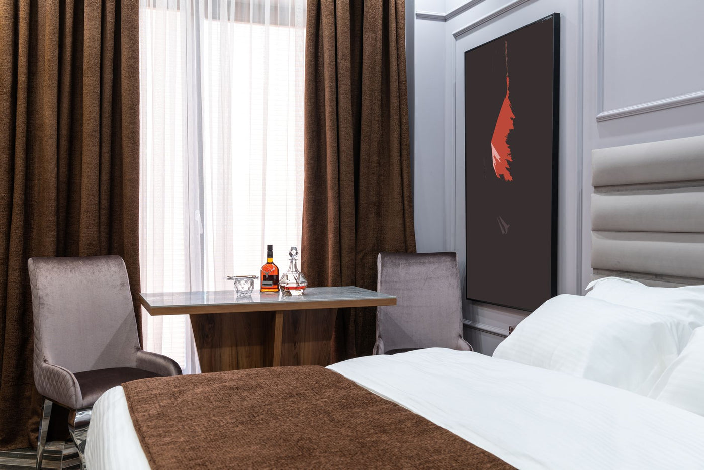 Soft bed against armchairs and table with carafe and bottle of liquor in light hotel room